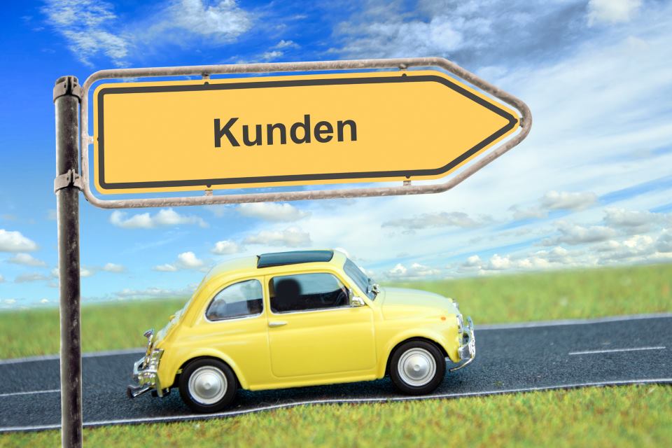 Gelbes Modellauto fährt an Schild vorbei mit Aufschrift "Kunden"